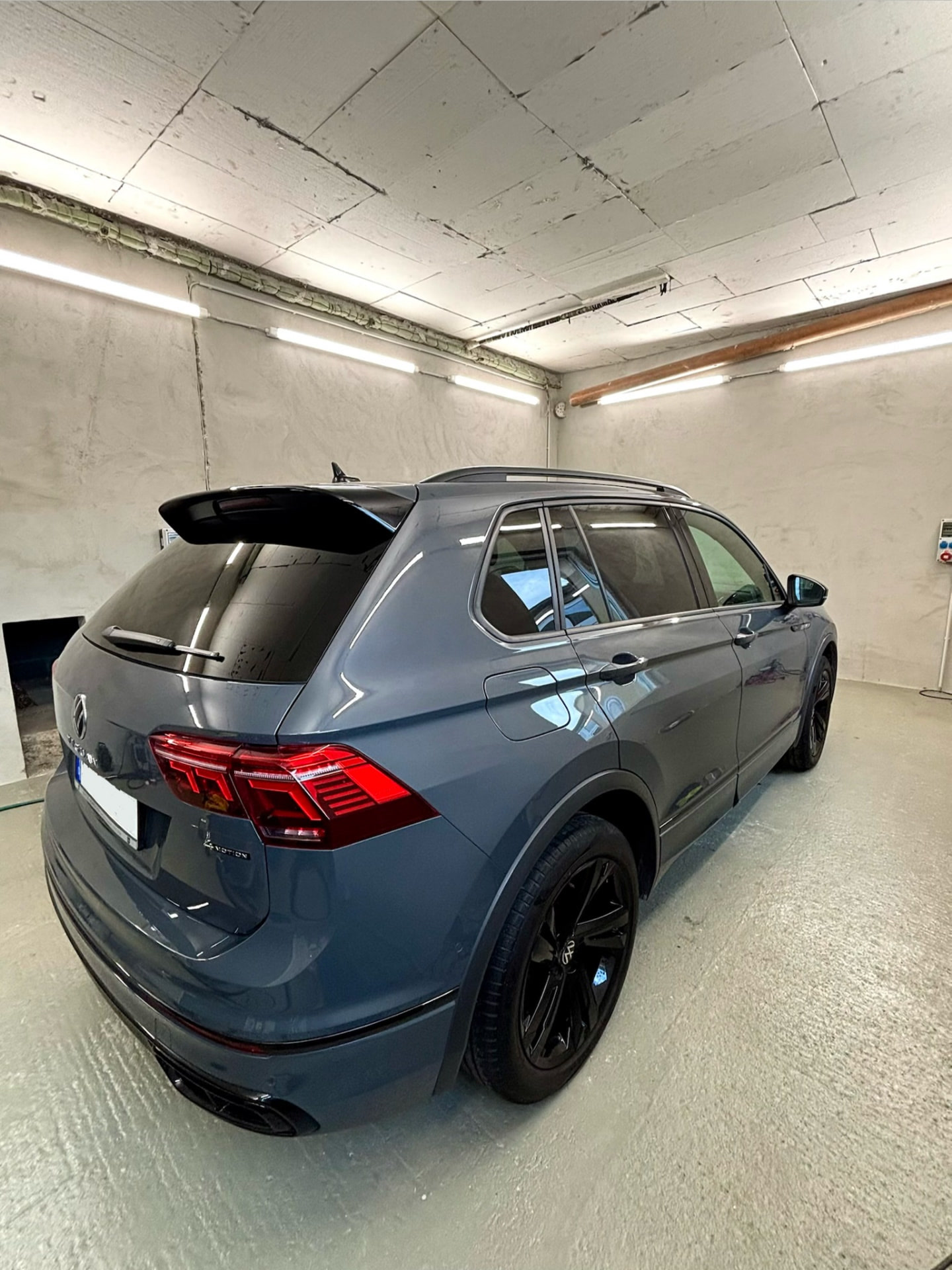 Graublauer VW Tiguan von schräg hinten in heller Werkstatthalle, glänzender Lack und schwarze Felgen
